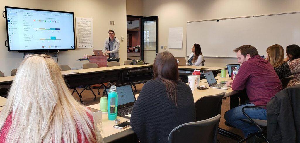 Tim, an Account Manager at Otus, leads a training at a client school in 2019. He stands at a podium in a room of six educators.