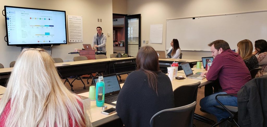 Tim, an Account Manager at Otus, leads a training at a client school in 2019. He stands at a podium in a room of six educators.